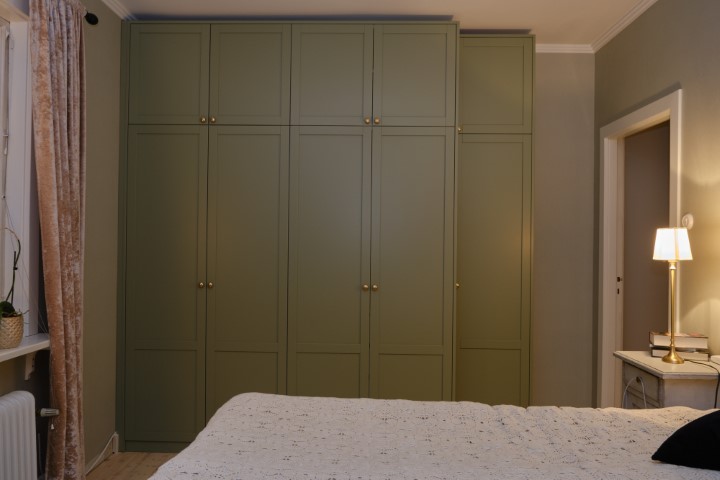 platsbyggd grön garderob med ramdörrar måttanpassad mot vägg och tak